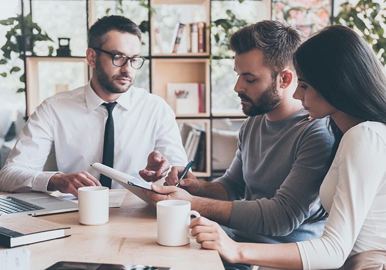 I need your signature. Confident young man signing some document while sitting together with his wife and man in shirt and tie